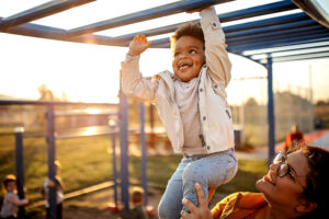 Kid playing on the monkey bars with mother in public park