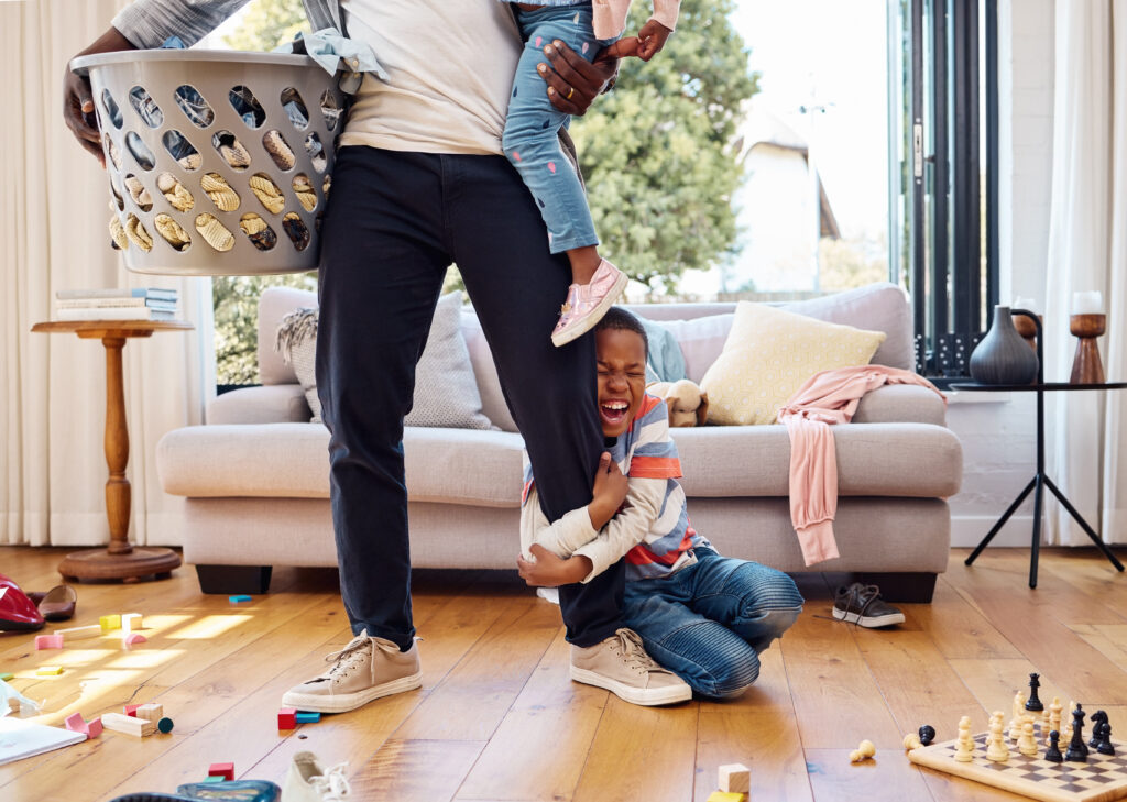 little boy throwing a tantrum while holding his parent's leg at home